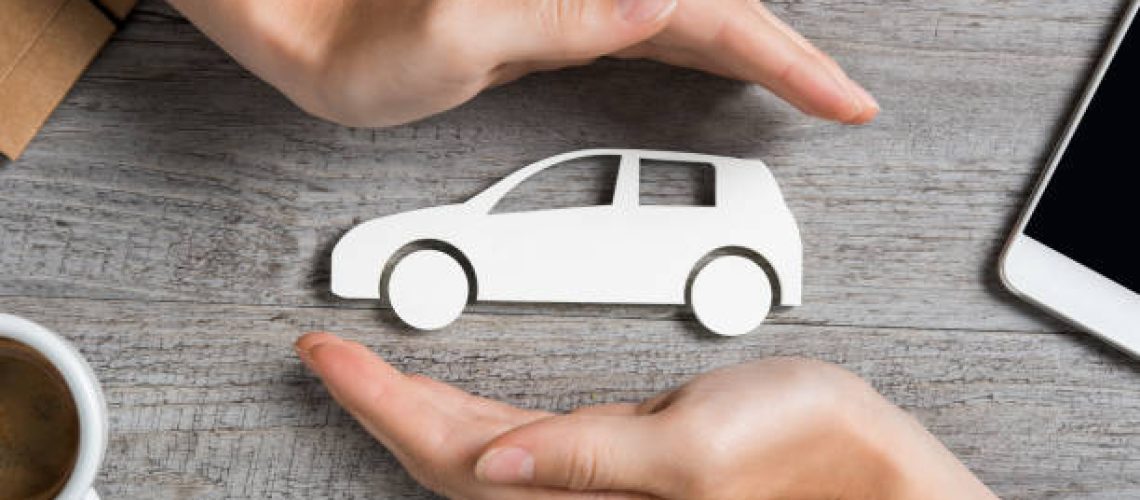 Hands protecting icon of car over wooden table. Top view of hands showing gesture of protecting car. Car insurance and automotive business concept.